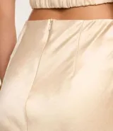 Vestido largo de satén color crema, con escote halter, espalda descubierta y abertura frontal. Presenta detalles de pedrería en el escote.