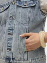 Chaleco de denim azul claro con cuello y cierre de botones, y bolsillos en el pecho.