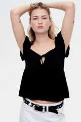 Top corto negro en punto arrugado con escote corazón, manga circular y sección cut-out con cordón para ajustar en el busto. Modelo ajustado sobre el busto con copas preformadas fruncidas y peplum con leve vuelo.