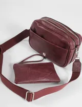 Cartera de hombro color bordó, confeccionada en cuero vegano, con un compartimento principal con cierre, un bolsillo frontal con cierre y un bolsillo trasero con cierre. Tiene una correa ajustable.