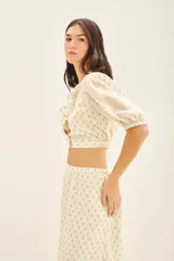 Top corto cruzado color crema con estampado de puntos dorados, escote en V con volados y mangas abullonadas al codo con puños elastizados.