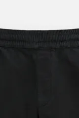 Bermuda color verde militar de corte relajado, confeccionada en tejido de algodón. Tiene cintura elástica ajustable con cordón interior, bolsillos frontales y bolsillo trasero de parche.