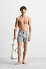 Short de baño con textura seersucker a rayas verticales azul marino y blanco. Tiene cintura elástica ajustable con cordón, bolsillos frontales y traseros, aberturas laterales en el bajo y forro interior.