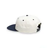 Gorra Vans de seis paneles color crema con visera azul marino y logo bordado en marrón.