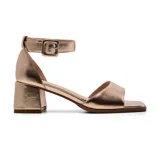 Sandalia de vestir color dorado, con tira ancha sobre los dedos, pulsera con hebilla al tobillo y taco cuadrado.