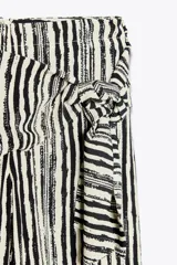 Pantalón de tiro alto con nudo delantero, de pernera ancha y estampado a rayas verticales en blanco y negro.