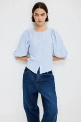 Blusa celeste y blanca a rayas verticales, de corte recto, con cuello redondo, cierre frontal con botones y mangas 3/4 abullonadas con puños elásticos.