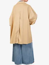 Gabardina color beige, de corte oversize, con cuello halter, cierre de botones y espalda con corte en el medio.