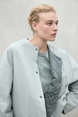 Chaqueta color crema con cuello redondo y cierre frontal con botones a presión.