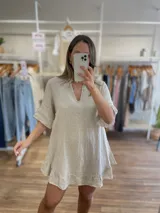 Vestido corto de lino color beige claro, con escote en V, mangas cortas con volados y ruedo con detalle de volado.