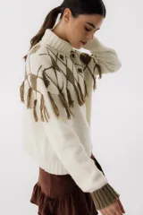Sweater tejido de punto color crudo con cuello alto y diseño de rombos marrones con flecos.