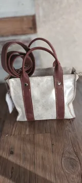 Bolso tipo tote de cuero plateado con detalles en cuero marrón. Tiene doble asa corta y correa larga extraíble.