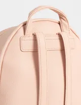 Mochila pequeña de cuerina color rosa pálido, con moño en relieve en el frente y llavero con forma de corazón trenzado. Tiene correas regulables, manija superior, cierre superior, bolsillo frontal con cierre y bolsillos laterales.
