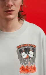 Remera color gris claro de corte oversize, con cuello redondo y mangas cortas. Estampado en la espalda con Mickey y Minnie Mouse sentados sobre una roca, con llamas y el texto 'Hello Darling'.