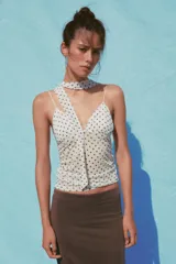 Top blanco con estampado de lunares negros, escote pico, tirantes finos y detalle de foulard en el mismo tejido.