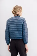 Campera azul de nylon con relleno de pluma, corte holgado a la cintura, cuello redondo y cierre frontal. Tiene bolsillos con cierre y detalle de vivos.