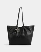 Cartera shopper negra de cuerina con manijas superiores y acceso mediante broche imantado. Incluye charm de perlas en forma de moño.