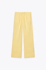 Pantalón de mujer color amarillo pálido, de corte ancho y tejido fluido. Tiene tiro medio, cintura elástica ajustable con cordones, bolsillos laterales y falsos bolsillos de vivo en la espalda.