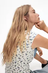 Top corto de punto acanalado fino de algodón color crema con estampado floral azul, mangas cortas y escote corazón con ribete de picot azul.