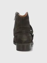 Bota corta de mujer color gris oscuro o marrón oscuro, estilo botín biker, confeccionada en gamuza. Presenta una tira decorativa con tachas metálicas plateadas y hebilla. Tiene un taco bajo y punta ligeramente afilada.