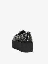 Mocasín negro de cuero con plataforma gruesa y apliques de tachas metálicas plateadas en toda la superficie superior y el borde de la plataforma. Presenta un detalle de hebilla metálica en el empeine.
