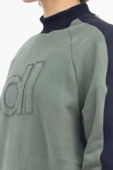 Buzo verde con cuello alto y mangas largas. Presenta un parche con letras en el frente y diseño color block en azul marino en la parte superior de la espalda y cuello.