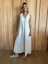 Vestido largo color crudo, sin mangas y con escote en V. Presenta aberturas laterales en el ruedo y bolsillos laterales a la altura de la cadera.
