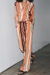Pantalón de tiro medio con estampado de rayas verticales en tonos marrón, naranja, rosa y beige. Cuenta con trabillas en la cintura, cinturón ajustable con lazadas, bolsillos laterales y cierre frontal con cremallera y botones.