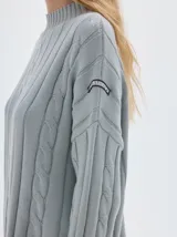 Buzo tejido color blanco, con cuello subido tipo polera, diseño oversized y largo con pequeños cortes laterales.