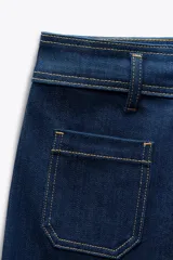 Pantalón de jean de tiro alto color negro con pierna ancha, bolsillos delanteros y traseros, y cierre frontal con cremallera y botón metálico.