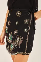 Minifalda negra con short interno, de corte cruzado con lazo lateral y bordados florales en frente y espalda.