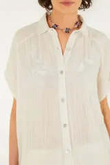 Camisa blanca de algodón con textura arrugada, corte holgado, mangas cortas, cuello clásico y cierre frontal con botones.