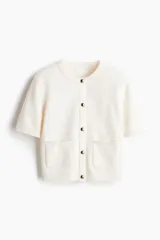 Cárdigan color crema de tejido de punto, con cuello redondo, manga corta, cierre frontal con botones metálicos y dos bolsillos delanteros.