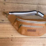 Riñonera negra con textura tipo piel de cocodrilo, con tres compartimentos con cierre y correa ajustable.