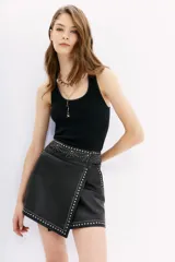 Minifalda negra cruzada de cuero ovino con apliques de tachas y piedras.