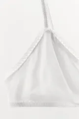 Bralette triangular gris de algodón con ribete de encaje blanco y detalle de moño rosa en el centro. Tiene tirantes finos ajustables y cierre trasero con ganchos metálicos.