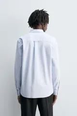 Camisa de algodón color celeste claro, corte regular fit, con cuello abotonado (button-down), manga larga con puño abotonado y bolsillo de parche en el pecho izquierdo.