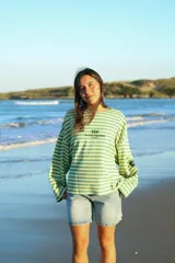 Buzo de manga larga con cuello redondo, reversible. Un lado es a rayas horizontales verde claro y verde oscuro, y el otro lado es liso verde oscuro. Presenta un estampado en la espalda con un logo de rayo y texto.