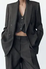 Blazer gris con diseño de líneas verticales, cuello solapa, manga larga con hombreras, bolsillos delanteros de vivo y cierre frontal cruzado con botones.