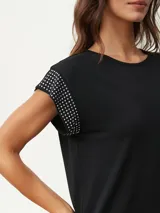 Remera negra de corte clásico con mangas cortas y detalle de tachas plateadas en los hombros.