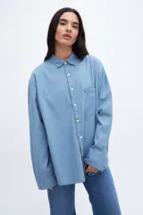 Camisa celeste de denim de algodón, con cuello solapa clásico, bolsillo cuadrado en el pecho, botones personalizados y calce oversize.