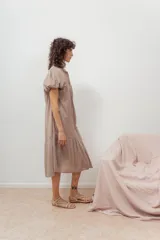 Vestido color beige con botones frontales, cuello camisero, mangas cortas abullonadas y falda con volantes.