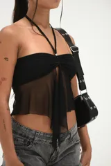 Top negro estilo bandeau con escote fruncido y detalle de lazo central. Presenta una capa inferior de tela transparente que cae en forma de lazo largo. Se sujeta al cuello con una tira fina.