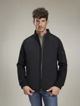 Campera azul marino con cierre frontal, cuello alto y bolsillos laterales con cierre. Tiene un parche rojo con cierre en la manga izquierda y un diseño acolchado en la parte delantera.