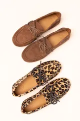 Mocasín tipo boat shoe con estampado de vaca en tonos marrón y blanco, confeccionado en cuero. Cuenta con cordones de cuero marrón oscuro y suela de goma.