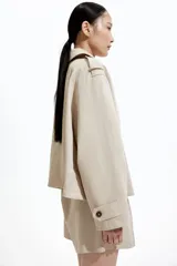 Chaqueta corta color beige, de corte oversized, con cuello clásico, charreteras abotonadas, bolsillos laterales y trabilla con botón en los puños.