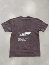 Remera oversize de manga corta, color marrón oscuro con efecto acid wash/lavado. Presenta un estampado gráfico en la espalda con un logo estilizado en forma de 'S' o espiral, cruces y texto que incluye "REAL / TRUTH IS A STATE OF MIND".