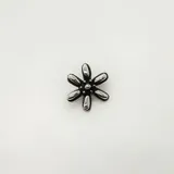 Dije con forma de flor con pétalos plateados y centro negro con pequeños detalles plateados.
