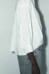 Camisa blanca de cuello solapa y manga larga con puños. Tiene un nudo en la parte delantera y cierre frontal con botones.