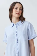 Vestido camisero corto de color celeste melange, con cuello camisero y mangas cortas. Presenta detalles de volados en el cuello, los puños de las mangas y a lo largo de la cartera de botones frontal. Posee un bolsillo tipo parche en el pecho y un corte holgado.